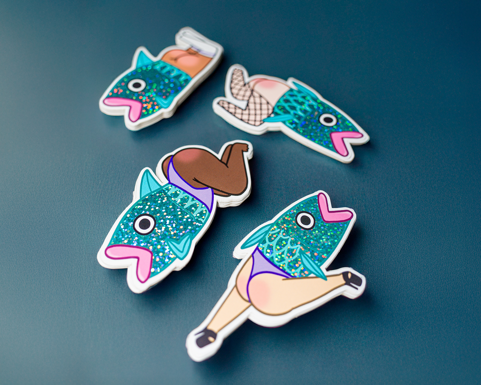 Four colorful Pixie Dust stickers of fish with human legs in various poses on a teal background.